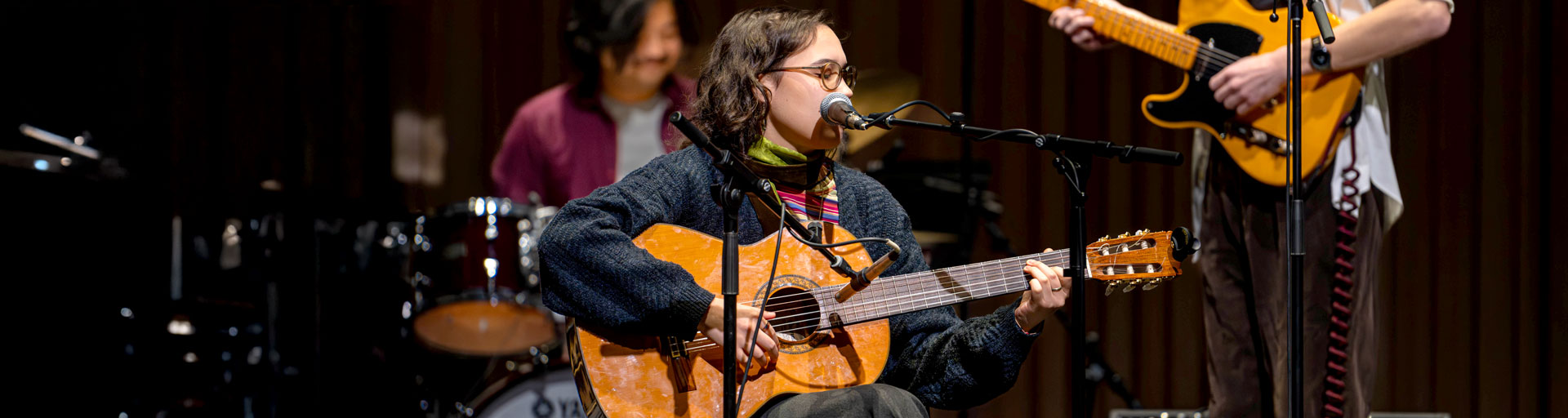 Person on stage playing guitar with two other musicians