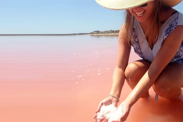 Student crouching in pink waters holding pink sand