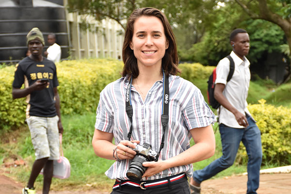 amanda smiling holding a camera with two men walking in the background