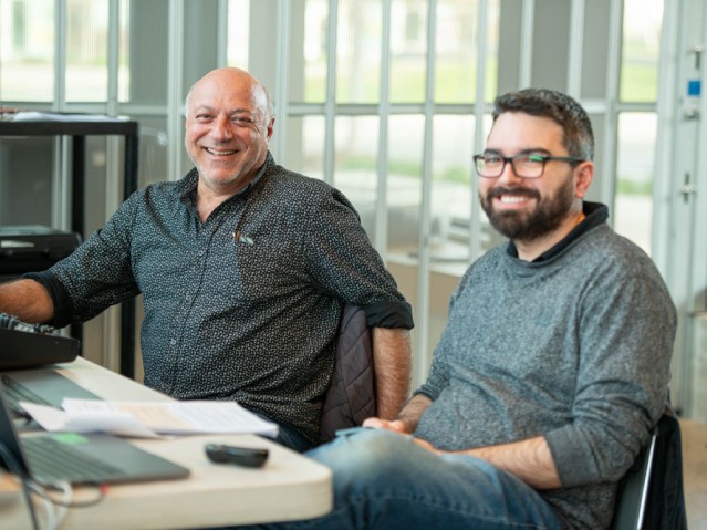 Two people sitting at desk smile for camera