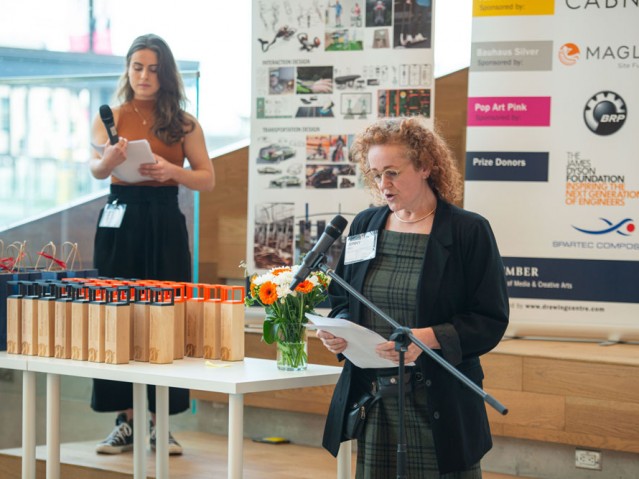 Person speaking into microphone beside awards table