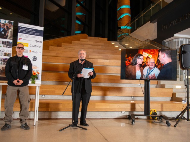 Two people standing in front presentation area, one behind the microphone