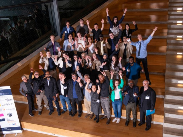 Group shot of Industrial Design students, faculty members, and event guests standing raising their hands