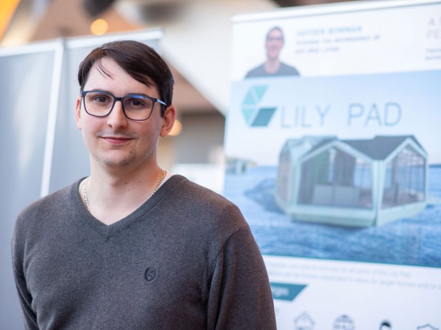 Student poses for photo in front of his project poster