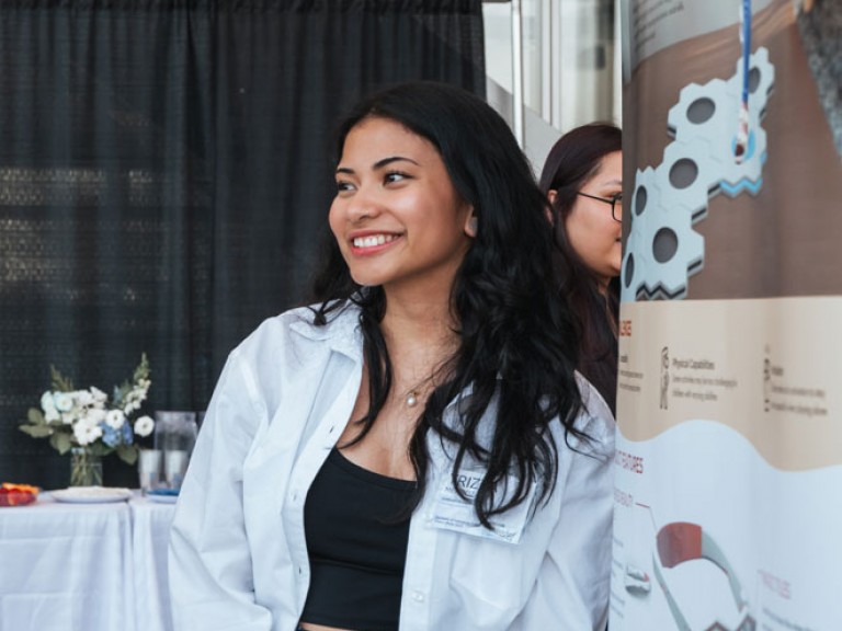 Design graduate smiling beside their poster
