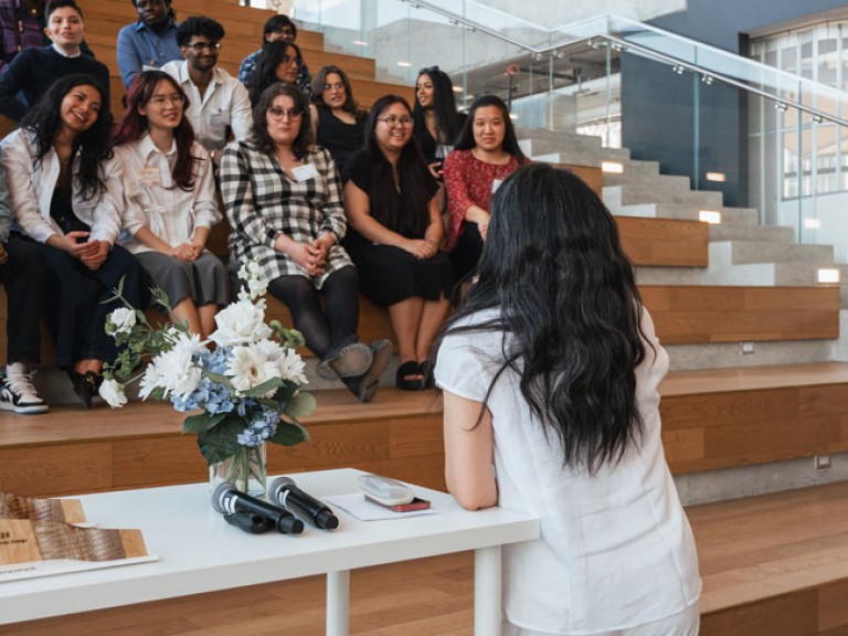 Person speaking to design graduates sitting on steps