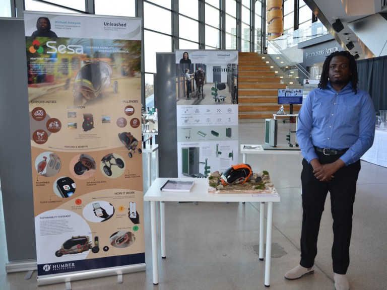 Industrial design graduate Michael Ameya standing beside his project display