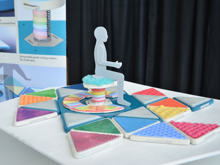 Physical 3D model of person sitting on stool on colorful floor pad design