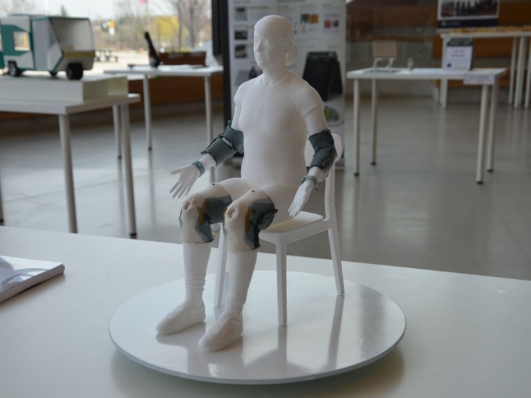 Physical 3D model of a sitting figure wearing elbow and knee braces