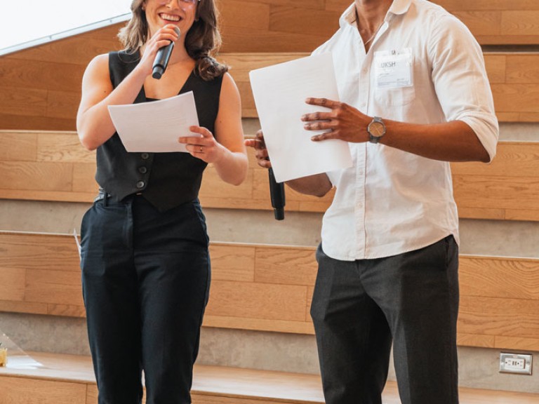 Two people standing with papers and microphones in hand