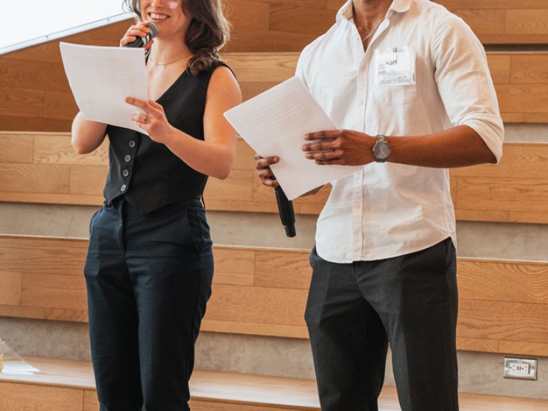 Two people standing with papers and microphones in hand