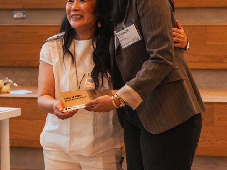 Design graduate and professor smiling for photo with award