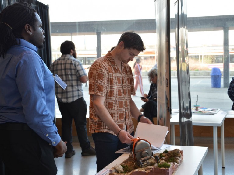 Design graduate and standing beside project table