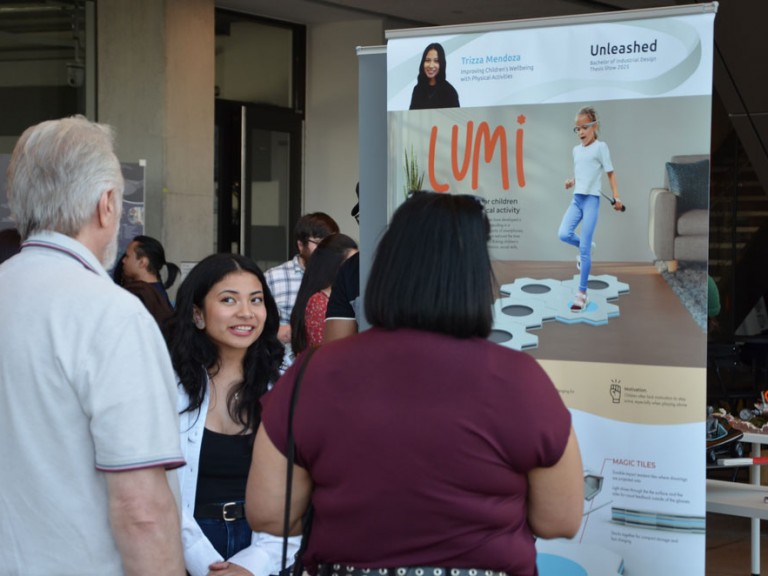Graduate Trizza Mendoza talking to guests in front of her project poster