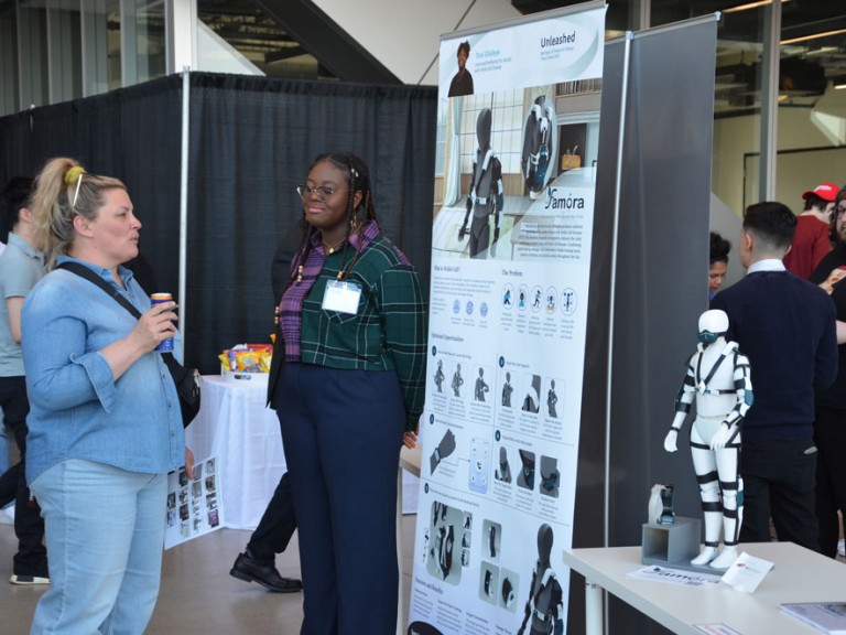 Graduate standing beside their project poster at event