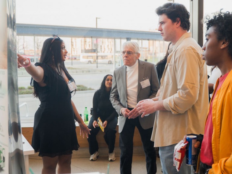 Industrial design graduate pointing at her project poster for three event guests