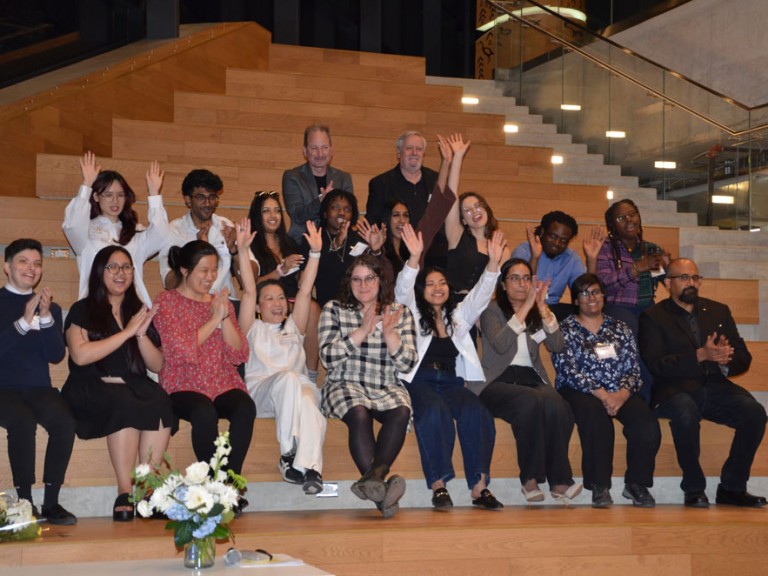 Group of people posing for photo on steps raising arms excitedly