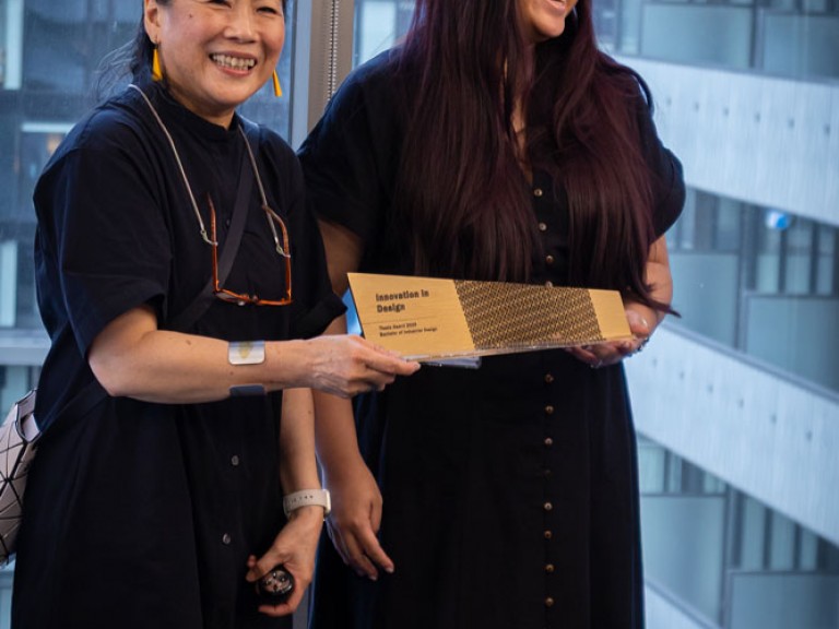 Industrial design graduate award winner and professor holding award and posing for camera