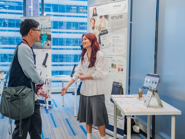 Design graduate in front of their project table talking to event guest